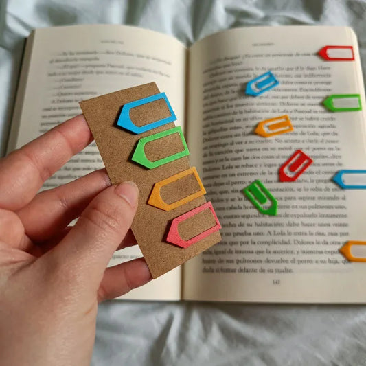 Set de 4 marcapáginas con forma de flecha en colores rojo, naranja, verde y azul, colocados en un libro.