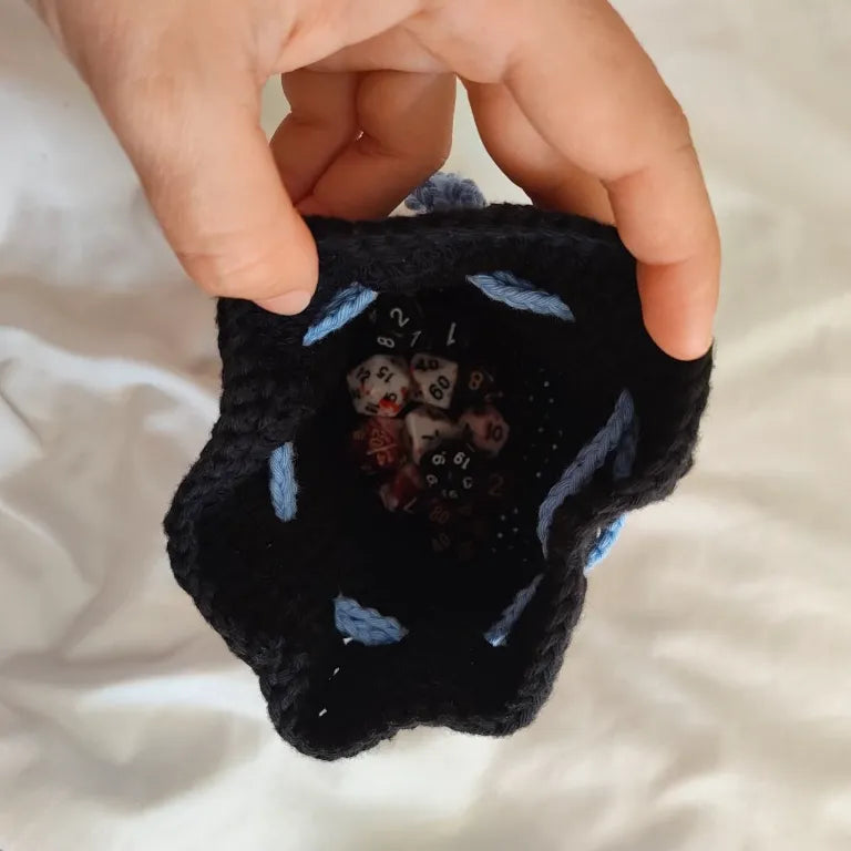 Vista cenital de la bolsa de dados negra de ganchillo abierta, enseñando el espacio de almacenamiento para juegos de mesa y rol.