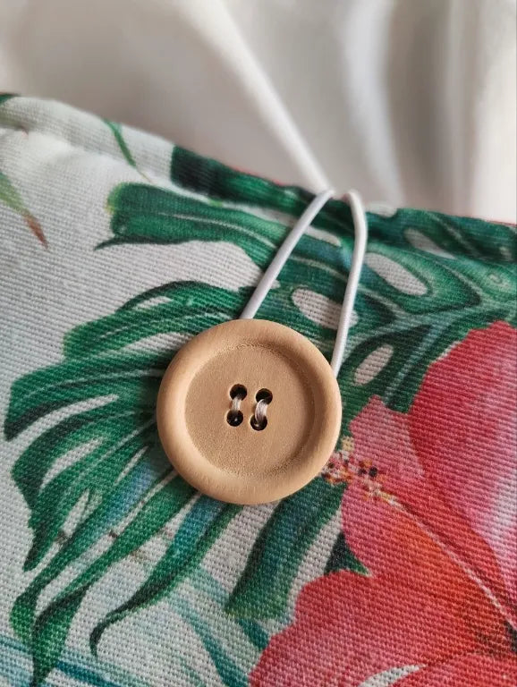 Primer plano del botón de madera natural y el lazo de cuerda elástica blanca utilizado como sistema de cierre en la funda botánica.
