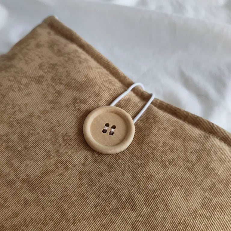 Detalle del cierre con botón de madera natural en la funda de tela Arena.