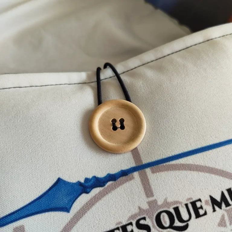 Detalle de cerca del sistema de cierre con botón de madera natural y cordón elástico.