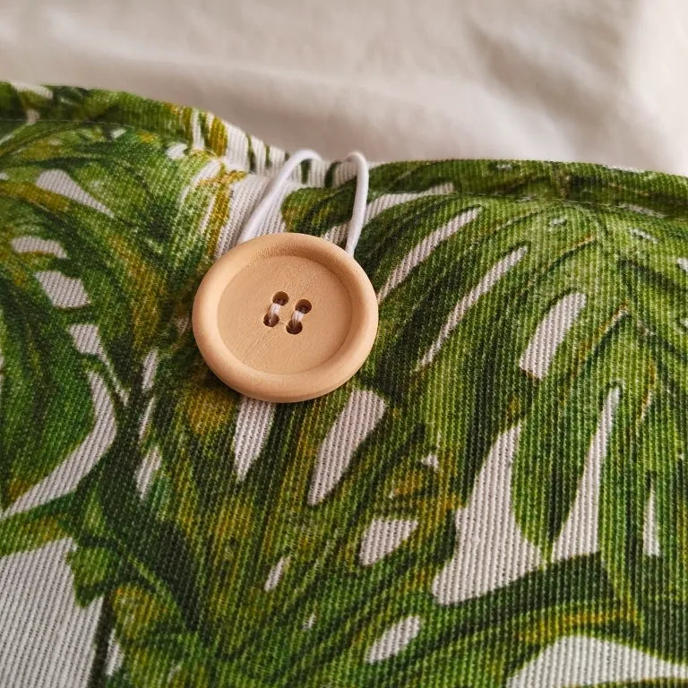 Detalle del sistema de cierre con botón de madera natural en la funda Monsterae.