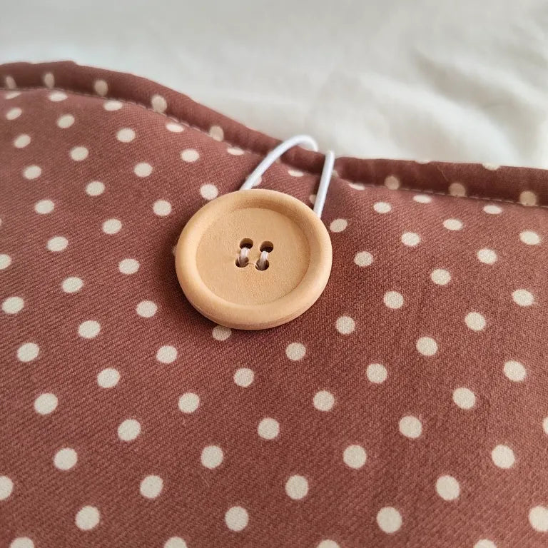 Primer plano del sistema de cierre con botón de madera natural y cordón elástico en la funda Moti.