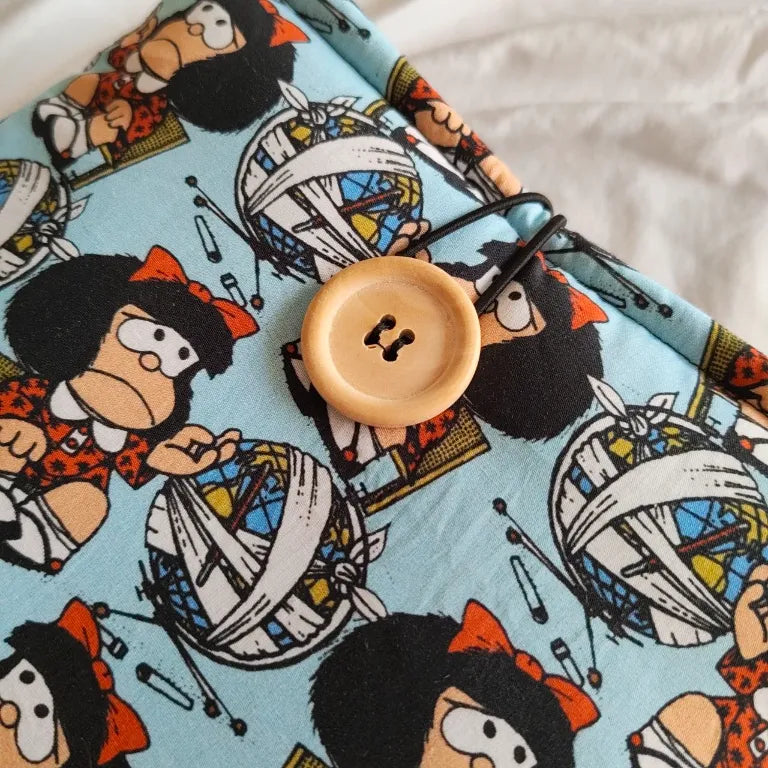 Primer plano en detalle del sistema de cierre con botón de madera natural y cordón elástico en la funda Quino.