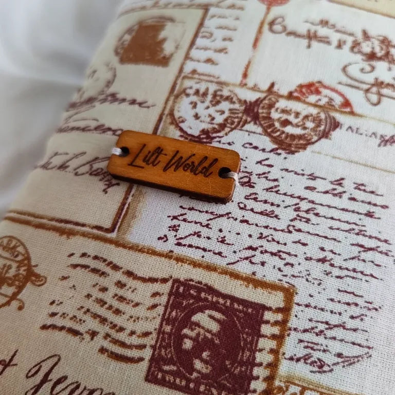 Primer plano de la etiqueta de madera de Lilt World sobre la tela de temática epistolar.