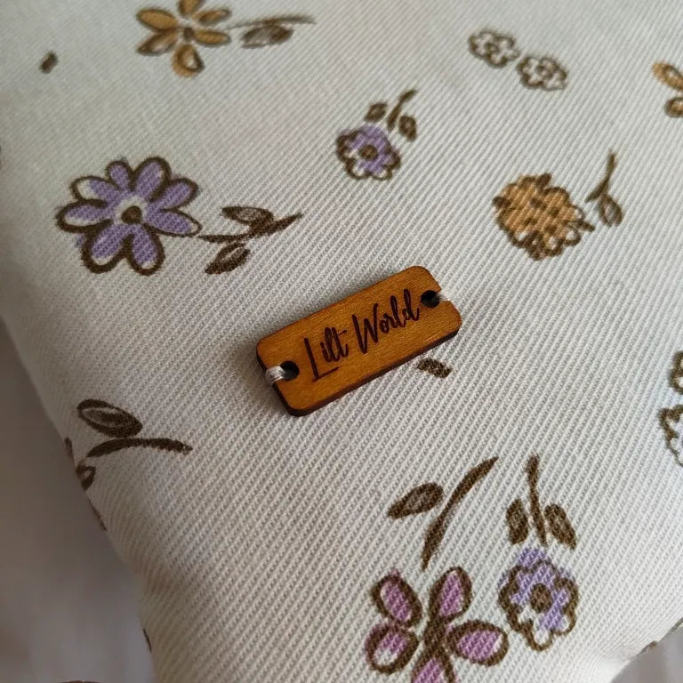 Primer plano de la etiqueta de madera de Lilt World cosida sobre la tela floral de la funda Nora.