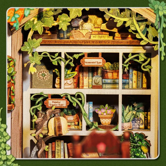 Primer plano detallado del interior de la maqueta, mostrando las estanterías blancas con libros ordenados por temáticas y plantas trepadoras en miniatura.
