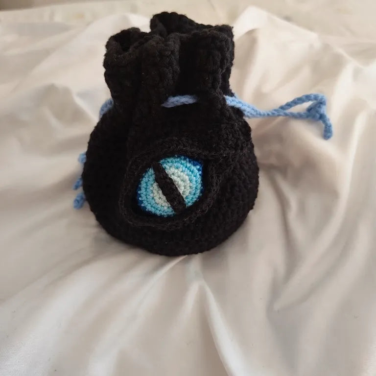 Bolsa protectora de dados en color negro con un intenso ojo de dragón helado en color azul cian y cordón a juego.