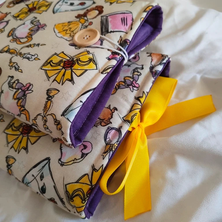 Dos fundas ¡Qué Festín! superpuestas, mostrando el forro interior acolchado en color morado y los cierres en botón y cinta amarilla.