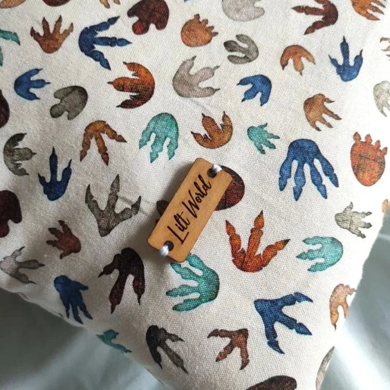 Primer plano enfocado en la textura de la tela con huellas multicolores y la chapa de madera con la marca Lilt World cosida.