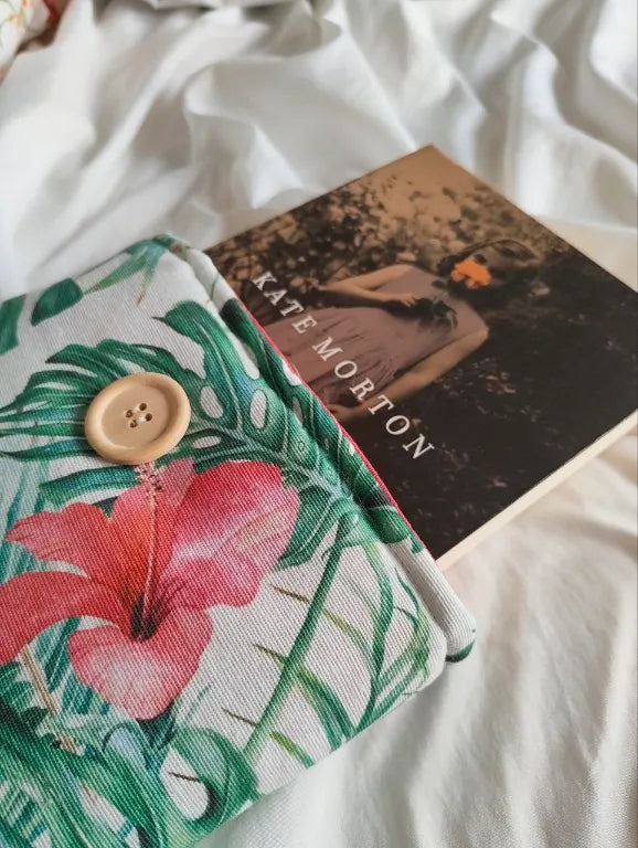 Funda para libro acolchada con estampado tropical hibisco siendo utilizada con un libro de tapa blanda de Kate Morton.