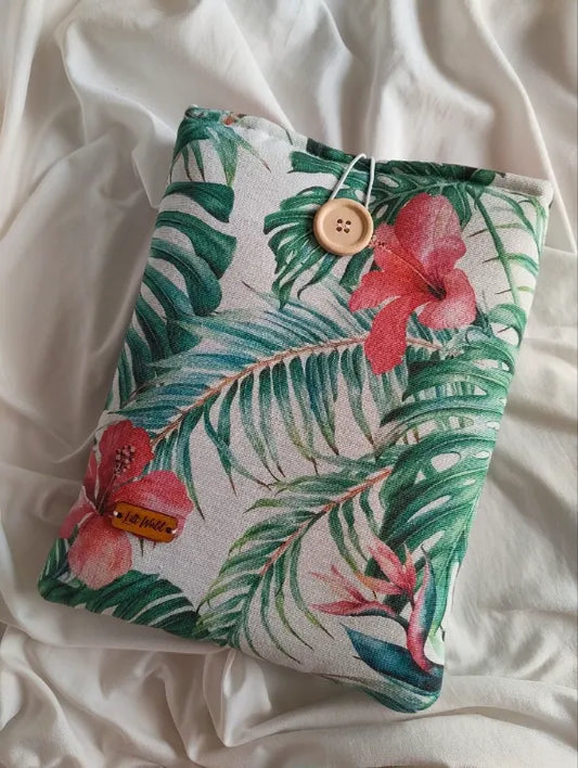 Vista completa de la funda para libro y Kindle "Hibisco" con su estampado floral tropical y botón de madera sobre fondo blanco texturizado.
