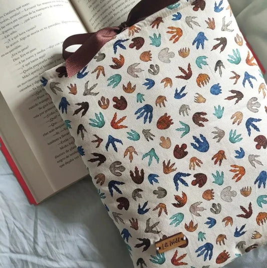 Vista frontal de la funda acolchada para libro y Kindle modelo Jurassic, con estampado de huellas de dinosaurio de colores y la etiqueta de madera de Lilt World.