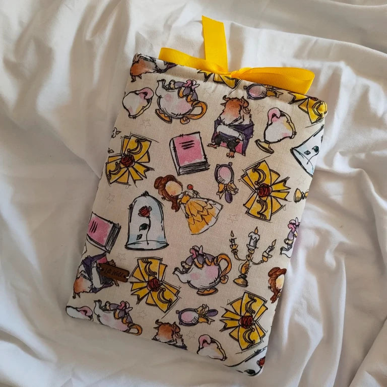 Vista frontal de la funda para libro y Kindle ¡Qué Festín!, con estampado de personajes y elementos de cuento, rematada con un lazo de raso amarillo.