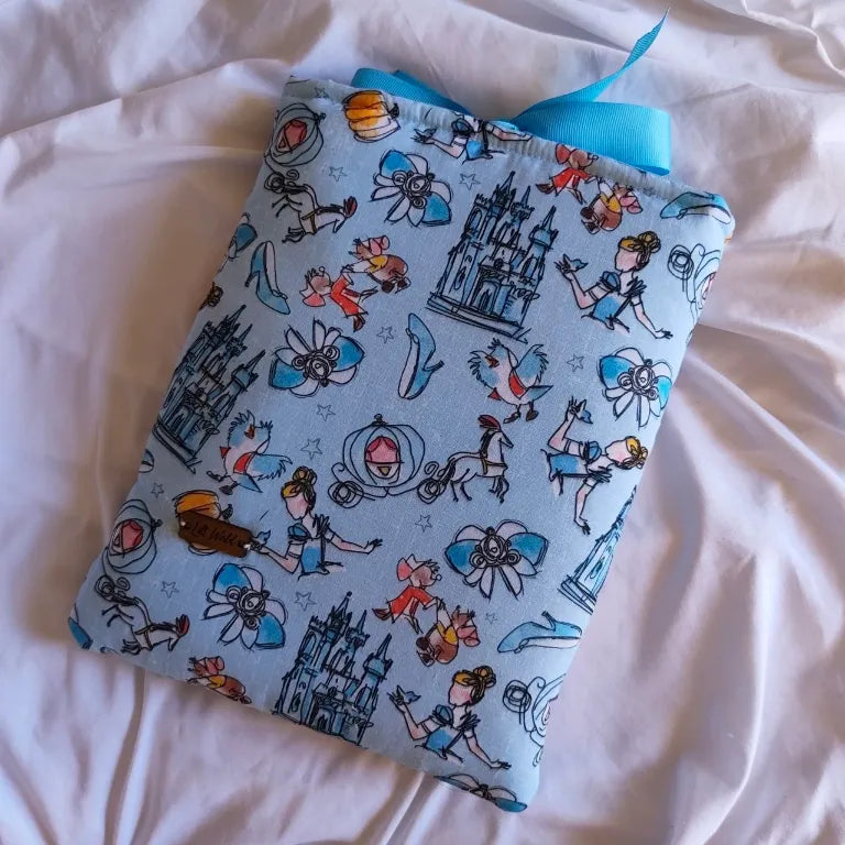 Funda acolchada para libro Cenicienta de tela azul con estampado de cuentos de hadas y etiqueta de madera.