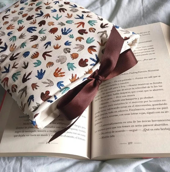 Plano cenital de la funda Jurassic sobre un libro abierto, mostrando el cierre con lazo de cinta marrón y la apertura acolchada.