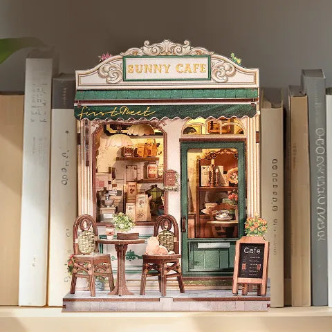 Diorama Sunny Cafe integrado como un book nook decorativo entre libros reales en una estantería de madera.