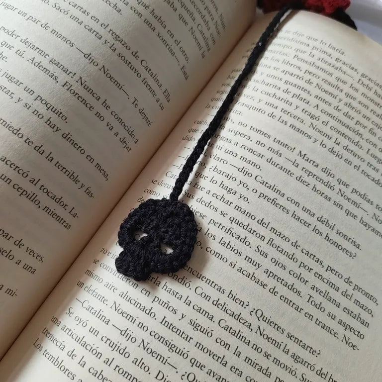 Primer plano de la calavera de crochet negra marcando el texto de un libro abierto.