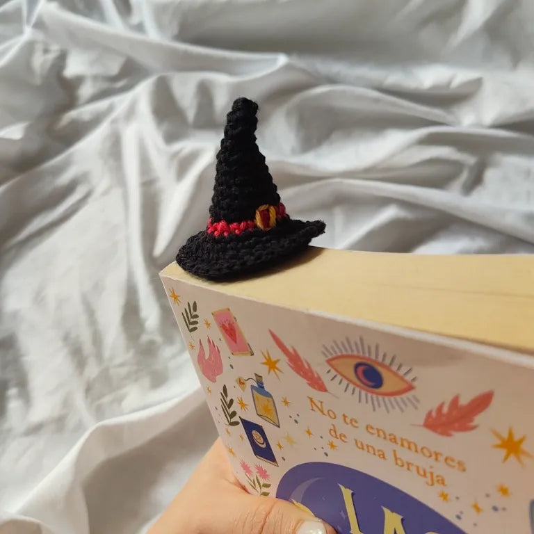 Vista superior del marcapáginas tejido con el sombrero de bruja asomando por la esquina superior del libro.