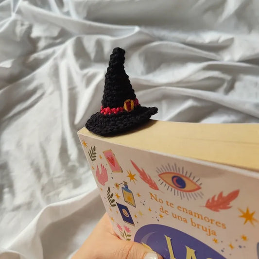 Vista superior del marcapáginas tejido con el sombrero de bruja asomando por la esquina superior del libro.