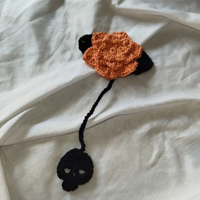 Marcapáginas de ganchillo con rosa en tono rosa claro y calavera negra desplegado sobre fondo blanco.