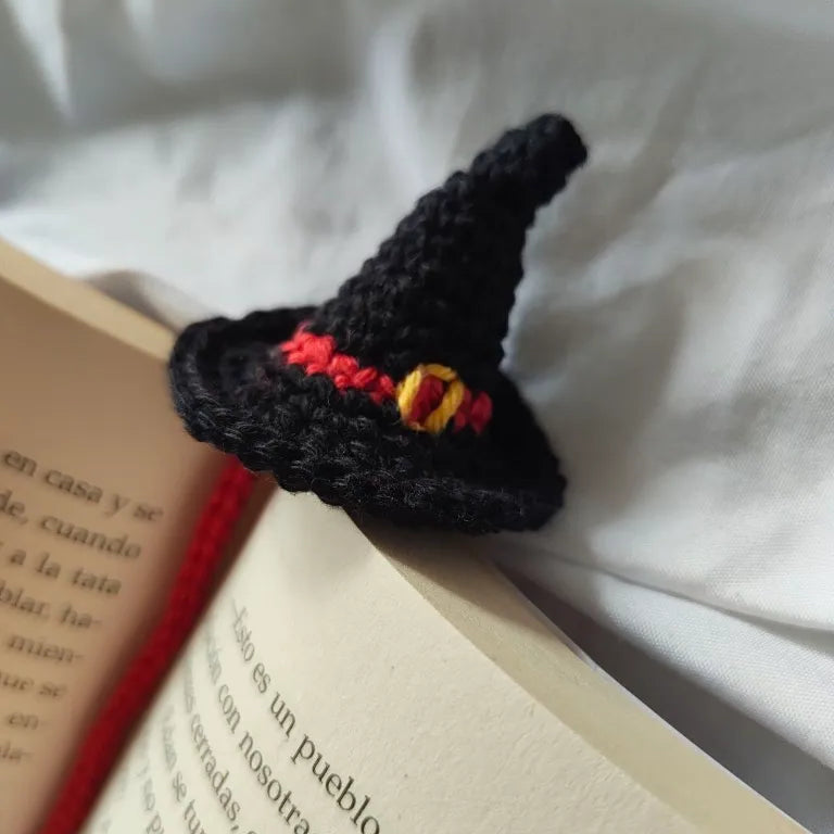 Primer plano en detalle del sombrero de bruja de crochet tejido en negro con cinta roja y hebilla dorada.