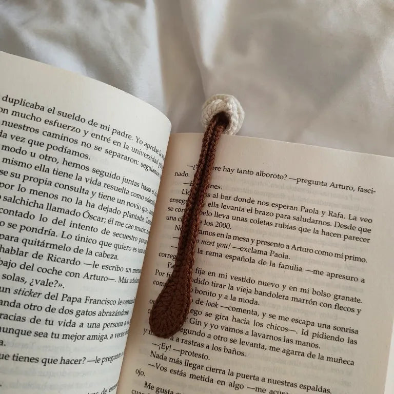 Marcapáginas de crochet con cuerpo tono café y taza tejida en beige sobre las páginas interiores de un libro abierto.