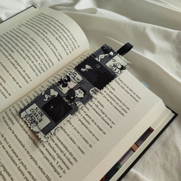 Marcapáginas de tela tipo esquinero con diseño de Snoopy Peanuts colocado en la esquina de un libro.